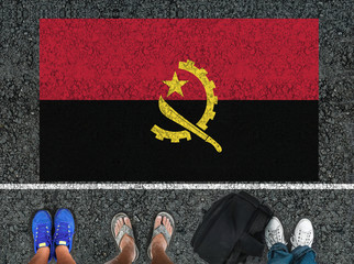 people legs are standing on asphalt road next to flag of Angola and border