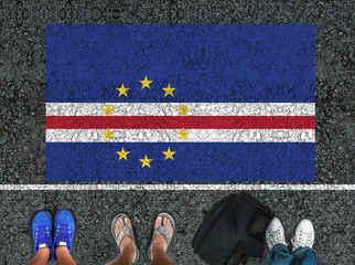 people legs are standing on asphalt road next to flag of Cape Verde and border