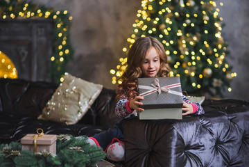 Obraz na płótnie Canvas Little girl sits on a sofa near a New Year tree