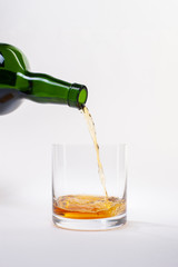 Pouring whiskey from bottle into glass with ice cubes on white background.