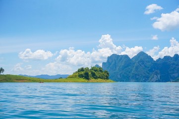 Fototapeta premium Beautiful view from Ratchaprapa dam in Thailand. Beautiful landscape view with blue water, blue clouds sky and mountains at the background. Tourists in the boat are enjoying the view