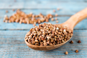 Uncooked buckwheat in a spoon on blue old boards. Buckwheat is used for cooking.
