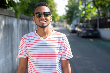 Happy young African bearded man with sunglasses smiling in the streets