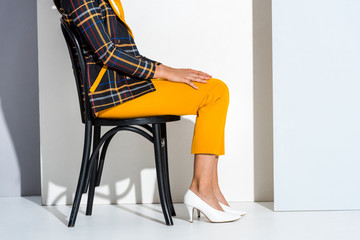 cropped view of young woman sitting on chair and posing on grey and white
