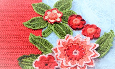 A group of crocheted flowers and leaves close up on decorative red and grey background