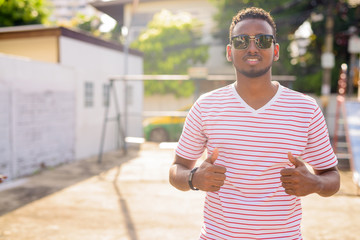 Happy young African man with sunglasses giving thumbs up outdoors