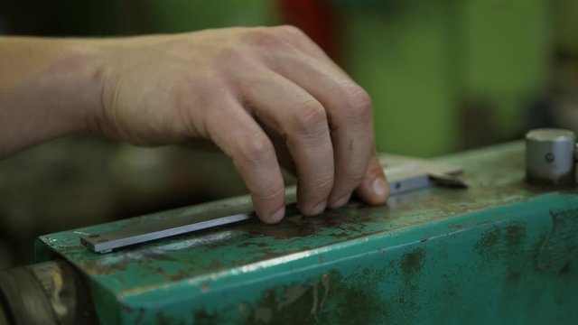 Iron slide gauge on a metal surface of some device. The hand of a factory worker is taking the sliding caliper.