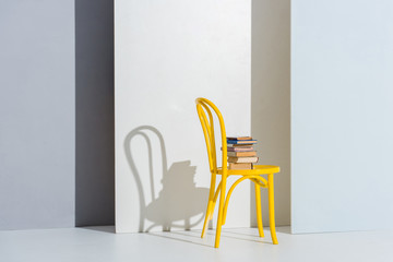 Fototapeta premium books on yellow chair on white and grey with copy space