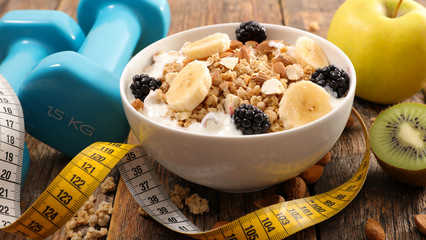 bowl of muesli with fruit, dumbbell and meter- fitness food concept