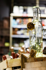 Empty bottle with burning garland and cones on blurred background .