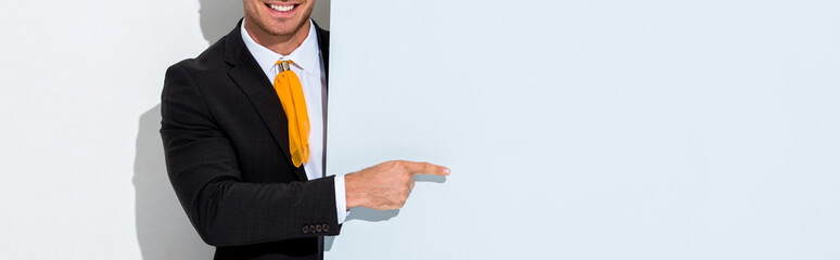 panoramic shot of happy man in formal wear pointing with finger on white