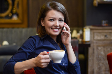 Young beautiful happy woman drinking coffee and talking on phone in cafe. business woman is reporting good news. lunch break in the office. coffee break, siesta. soft focus