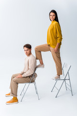 cheerful girl standing on chair near handsome man sitting on white