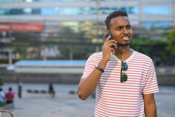Happy young African bearded man talking on the phone in the city