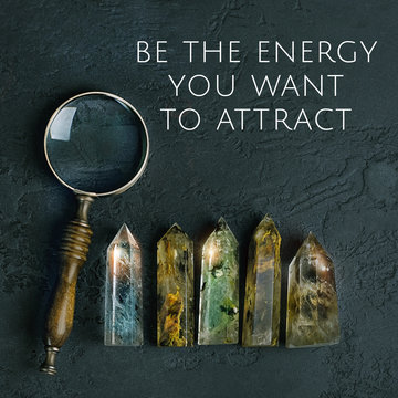 be the energy you want to attract - inspiration quote.  composition with magnifying glass and quartz stones mineral. gemstones crystal for relaxation on abstract black background