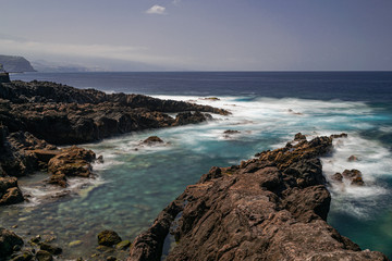 Volcanic rocks coastline with afternoon sunlight, blue Atlantic Ocean with waves foam, long exposure, Rojas, El Sauzal, Tenerife, Canary islands, Spain