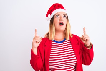 Young beautiful woman wearing Christmas Santa hat over isolated white background amazed and surprised looking up and pointing with fingers and raised arms.