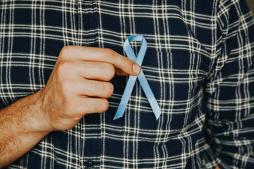 Man's hand holding a blue ribbon simbol of Movember prostate cancer awareness month. Men's cancer...
