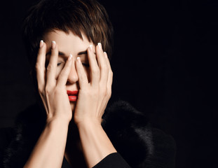 Portrait of grieving woman with closed eyes covering her face with her hands, hiding on dark background