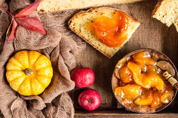 Round loaf of artisan wheat bread with pumpkin and apple in a wooden tray. Autumn composition with jam, decorative small pumpkins, apples and wheat ears. Selective focus. Rustic style.