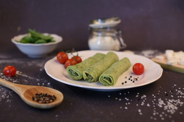 Spinach pancakes stuffed with white cheese. Composition on a dark background