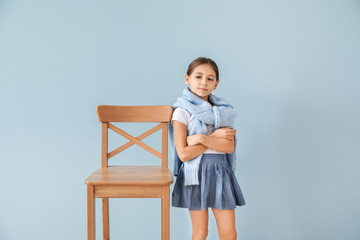 Cute fashionable girl with chair on color background