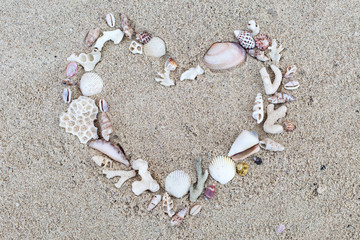 Fototapeta na wymiar Seashells and corals heart frame on sand background.