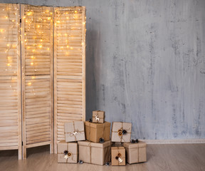 heap of christmas gifts and folding screen with lights - copy space over concrete grey wall