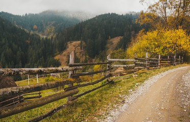 Fototapeta na wymiar Dirt road with a wooden fence in the background of mountains in the distance under a cloudy sky with fog