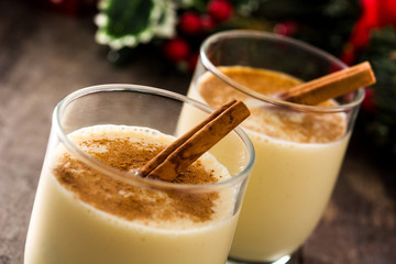 Homemade eggnog with cinnamon in glass on wooden table. Typical Christmas dessert..