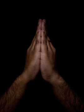 low key photo of a brown man with hands placed together showing the sign of namaste, the indian way of respectful greeting