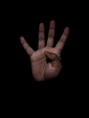Low key photo of a brown man showing the number four with his fingers