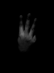 Low key black and white photo of a man showing the back of his hand with his three fingers sticking...