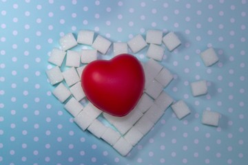 Protect your blood vessels and heart.Heart created from white sugar cubes on blue background with white polka dots. Red heart lies on sugar.