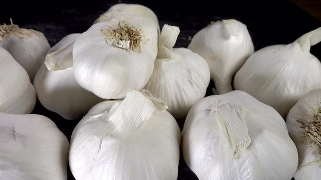 Close POV slow pan shot across whole garlic bulbs / heads in a group, with fingers picking one from the end. 