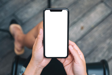 Top view mockup image of a woman holding a black mobile phone with blank white desktop screen