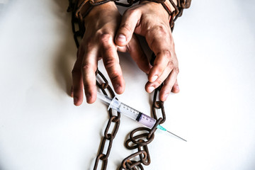 Man's hands in old rusty chains near the syringe with needle. Addicted to drugs. Dangerous habit.