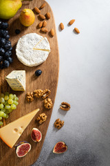 Cheese plate served with camembert, brie, blue cheese, maasdam, grapes, pear, figs and nuts on a wooden board on gray background. Top view, flat lay. Copy space. Dairy products, keto diet