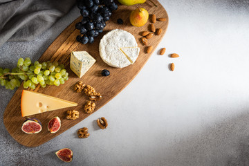 Cheese plate served with camembert, brie, blue cheese, maasdam, grapes, pear, figs and nuts on a wooden board on gray background. Top view, flat lay. Copy space. Dairy products, keto diet