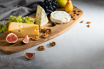 Camembert, brie, blue cheese, maasdam, grapes, pear, figs and nuts on a wooden board on gray background. Side view, copy space. For banner, menu. Healthy food, nutrition concept