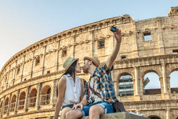 Lovely couple of tourist sitting on a wall kissing at Colosseum while taking selfies. Rome, Italy