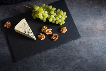 Tasty blue cheese served with green grapes and walnuts on a black stone board. Dorblu cheese...