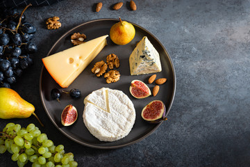 Cheese plate. Assortment of cheese with nuts and fruits on wood serving board over gray concrete texture background. Top view with copy space. Appetizer theme, keto diet