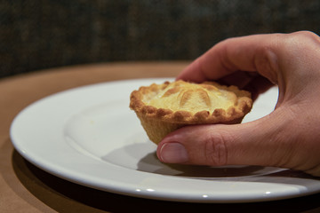 Hand of woman taking Christmas mince pie. Fruit mince pies for festive, winter season.  Mince pie on white plate. Holidays concept. Selective focus. Delicious.