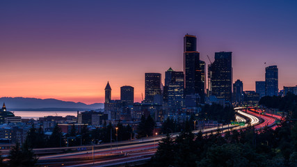 Fototapeta na wymiar Seattle skyline, at sunset. The cars along the highway are creating light trails, due to a slow shutter speed