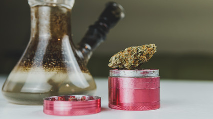 Close-up of dirty bong and grinder with medical marijuana buds on the white table. Smoking cannabis...
