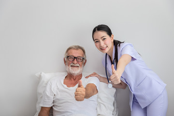 Happy nurse and elderly man in bedroom at nursing home, thump up, looking camera