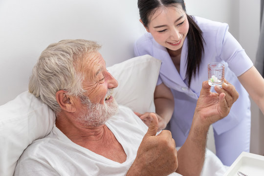 Happy nurse give pills, assist, and encourage elderly senior man to eat medicine after breakfast on bed in bedroom at nursing home