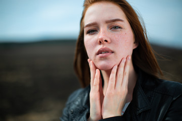 Stylish redhead girl puts her fingers to her face and looks at us. - obrazy, fototapety, plakaty