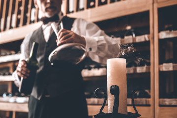 Sommelier Concept. Senior man standing with wine bottle and decanter looking at blew out candle close-up